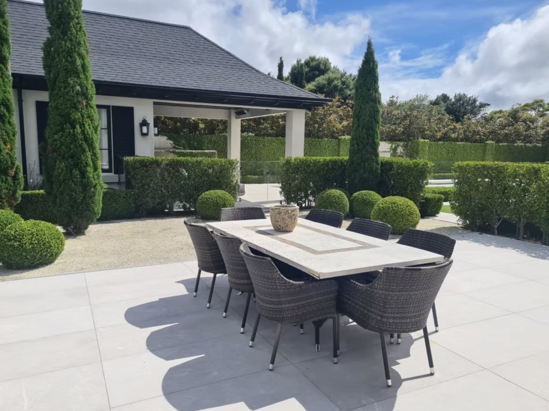 A formal residential garden with clipped topiary and outdoor dining